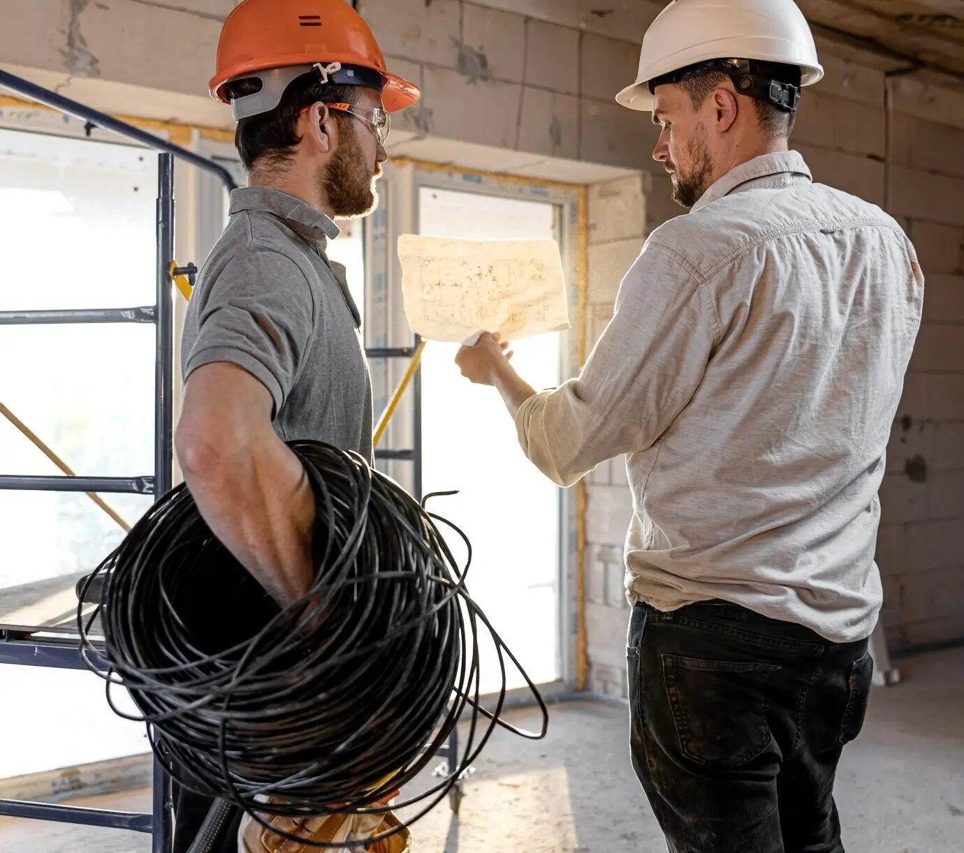 Two building engineers talk at a building site, with one engineer explaining a drawing to a worker.